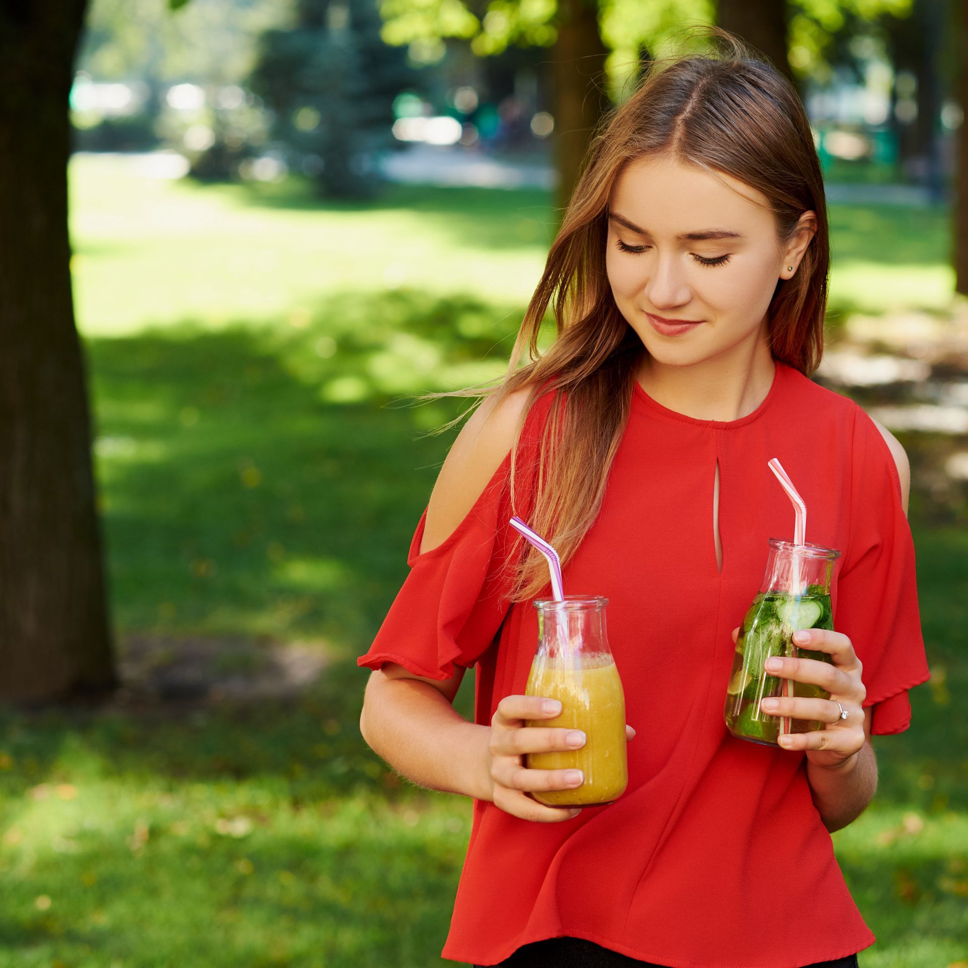 Woman in red top holding two drinks outdoors.