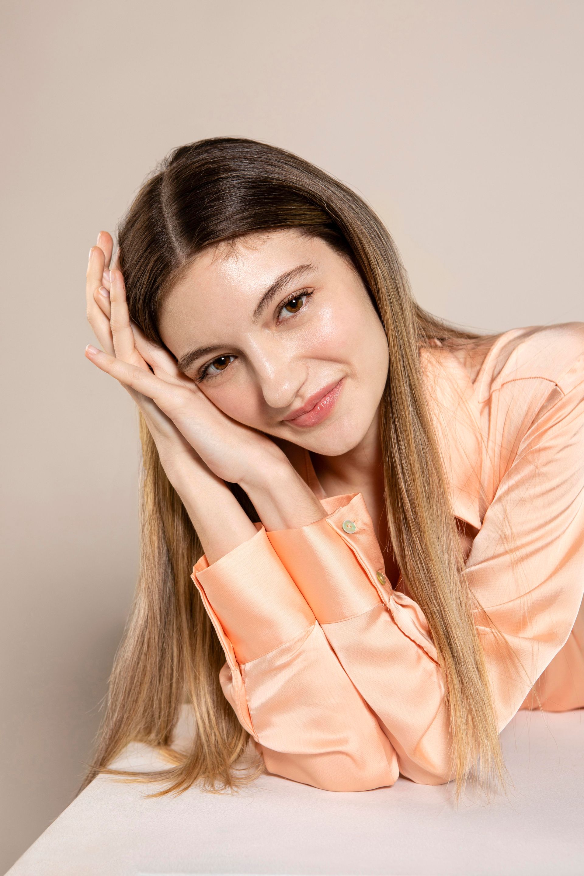 A woman in a pink shirt is sitting at a table with her hands on her face.