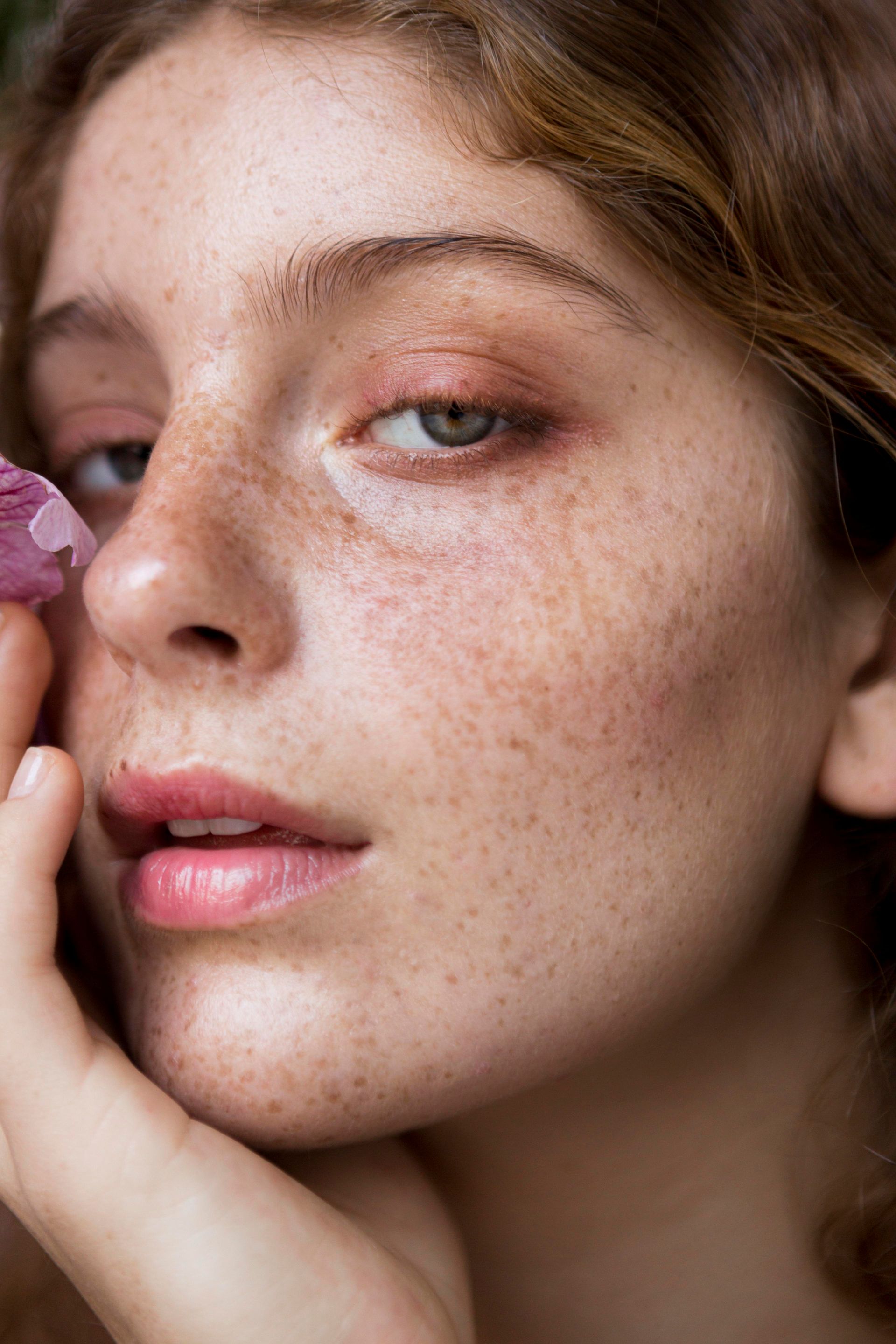 A woman with freckles is holding a purple crystal in front of her face.