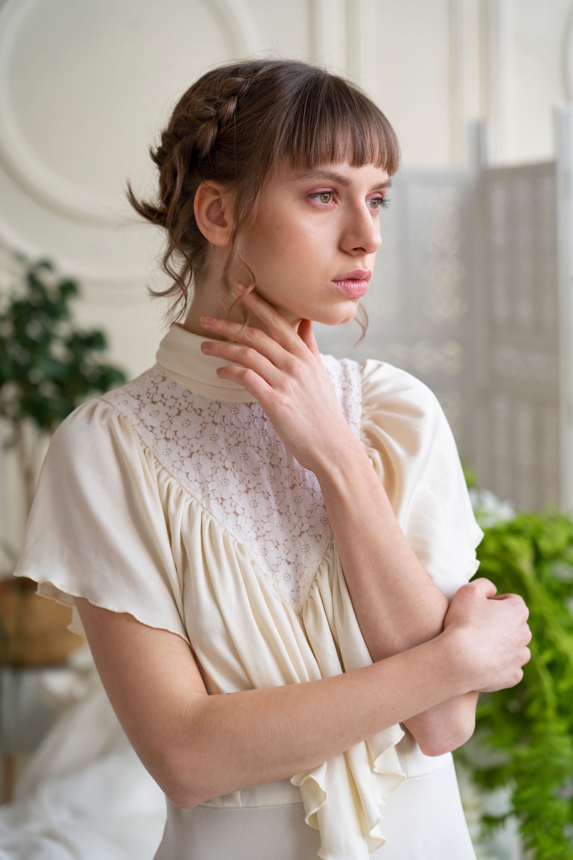 A woman in a white dress is standing in a room with her hands on her face.