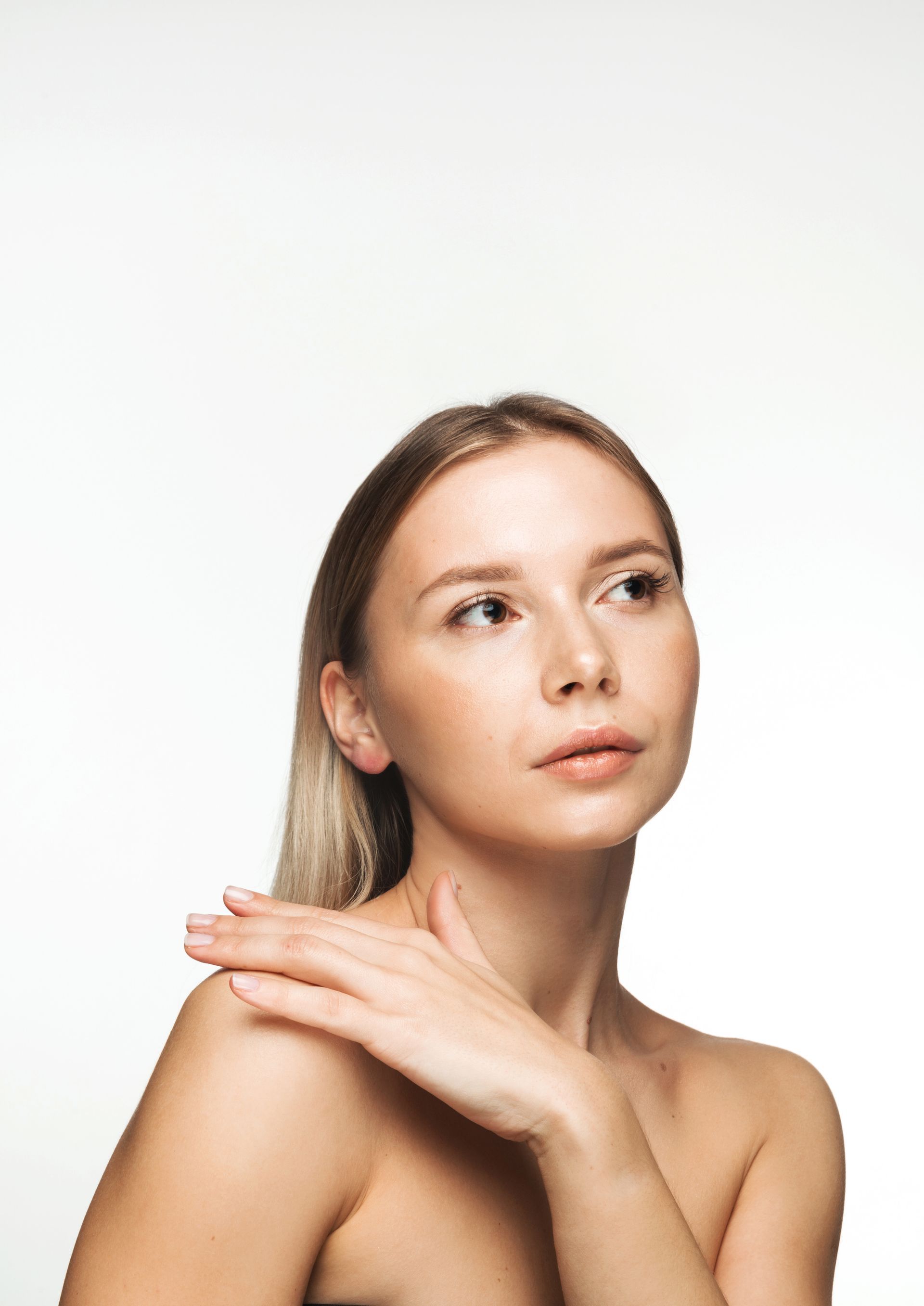 A woman without a shirt is holding her hand to her neck and looking up.