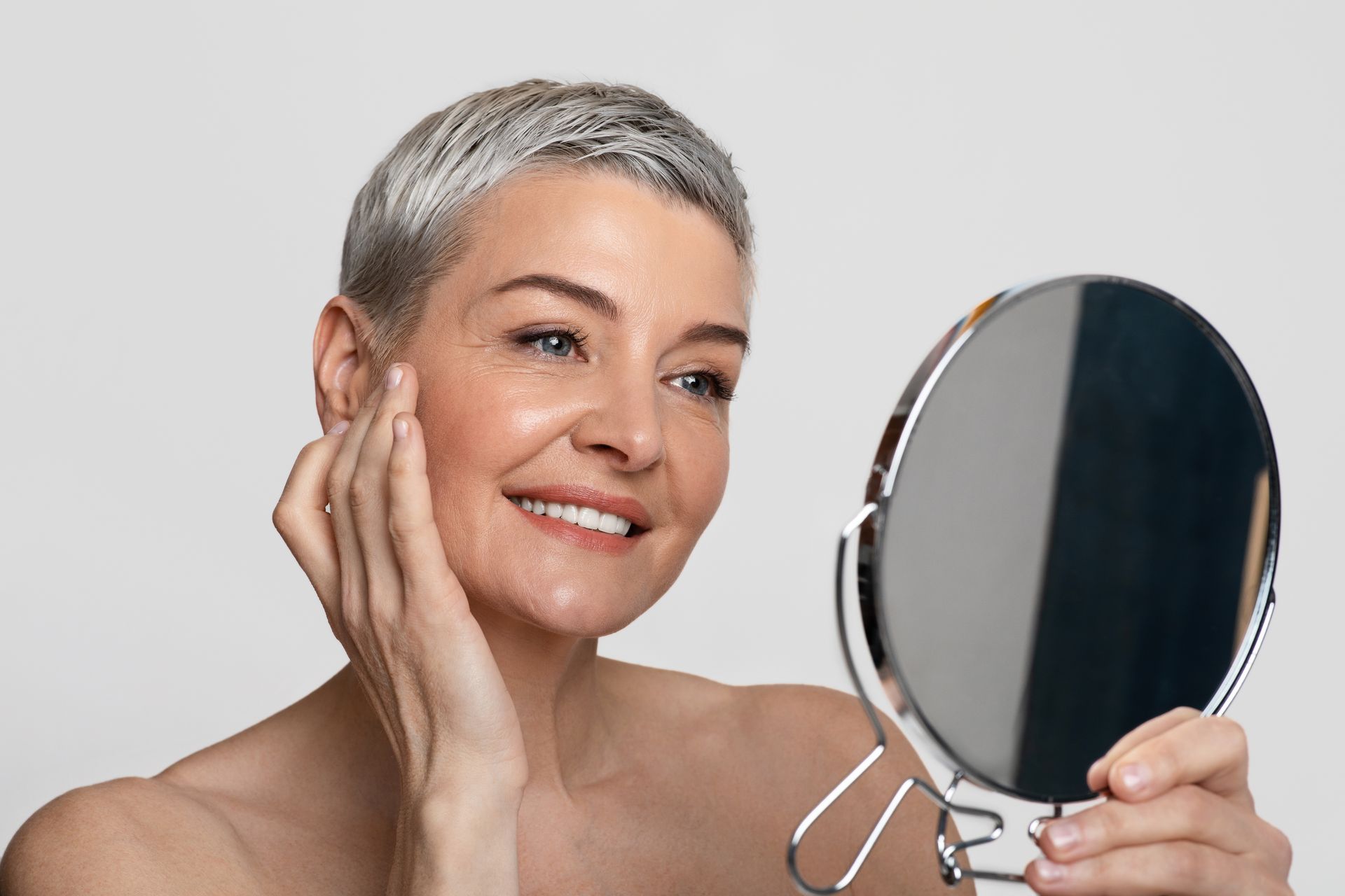 A woman is looking at her face in a mirror.