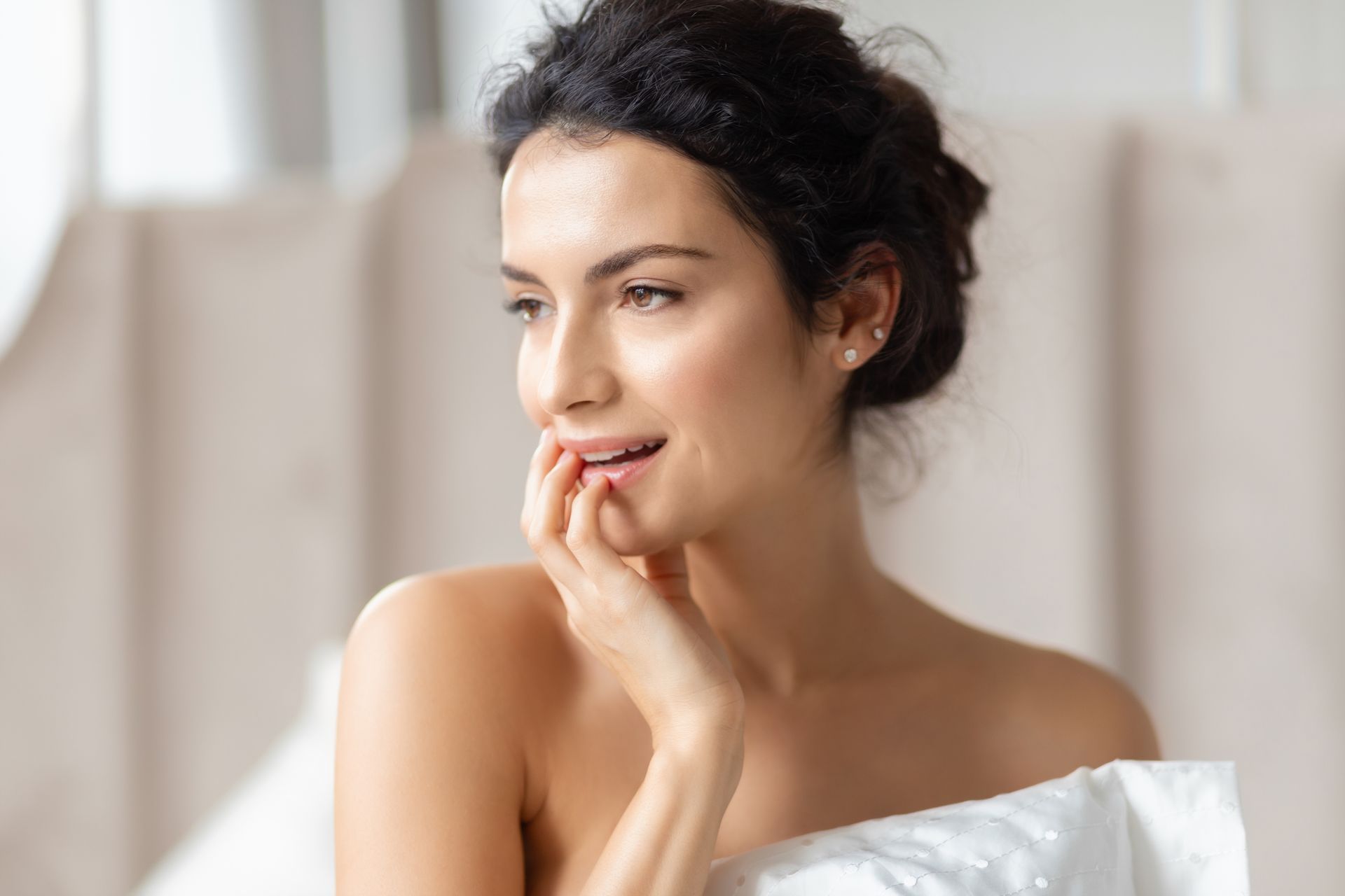 A woman is sitting on a bed with her hand on her face.