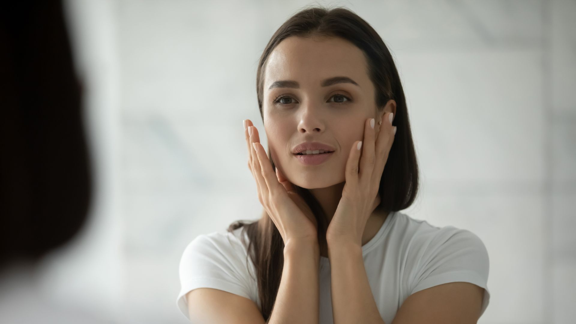 A woman is looking at her face in the mirror.