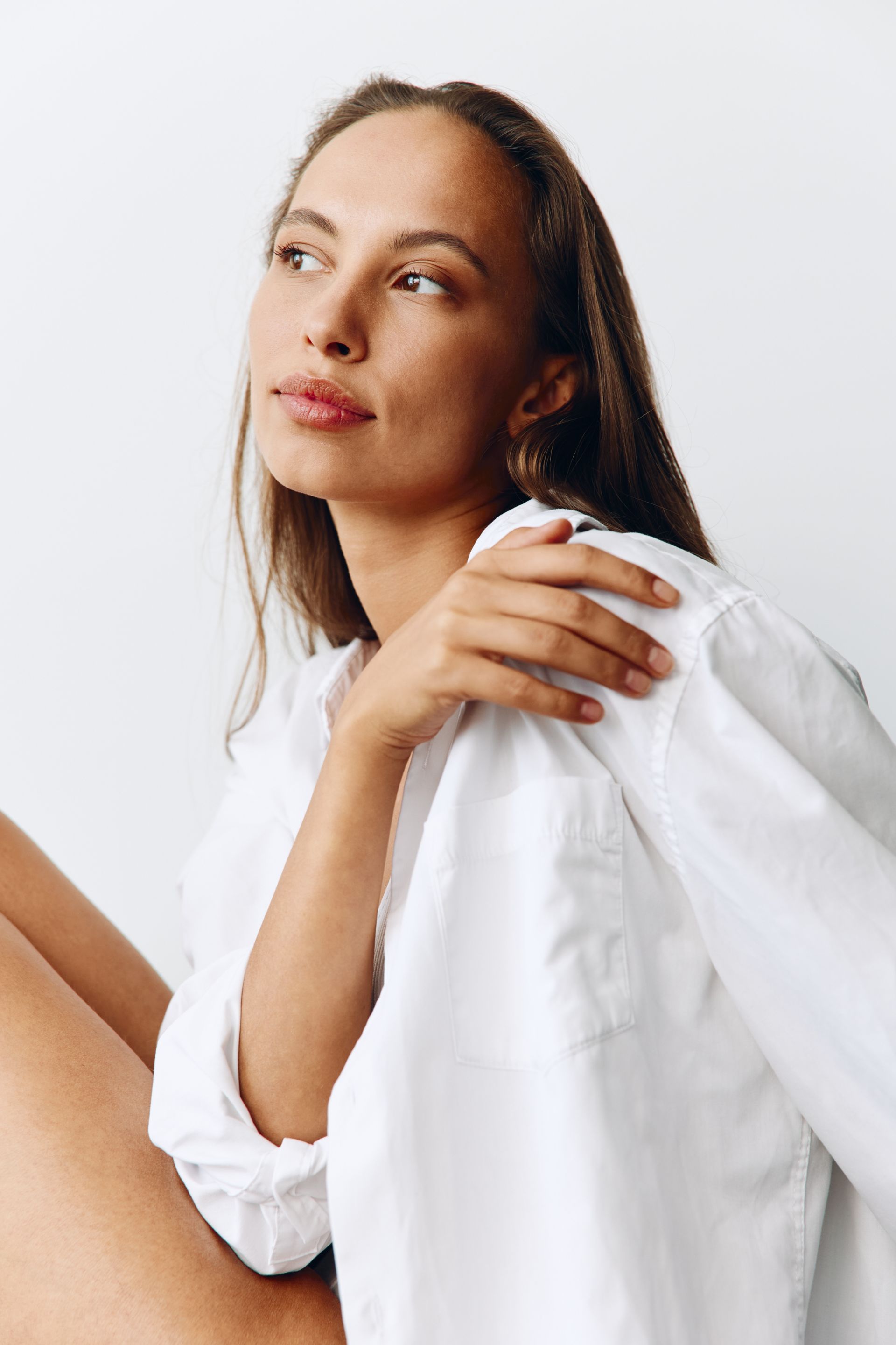 A woman in a white shirt is sitting down with her legs crossed.