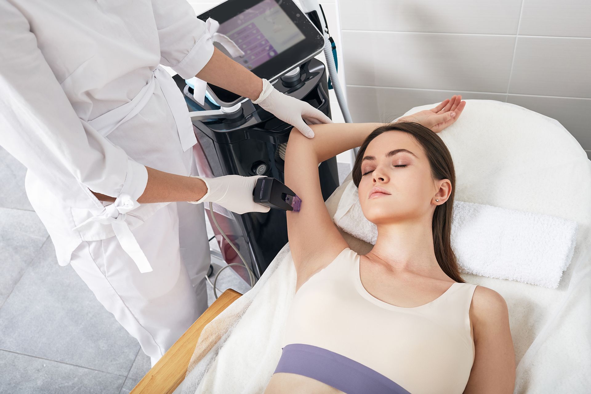 A woman is laying on a bed getting her armpit hair removed.