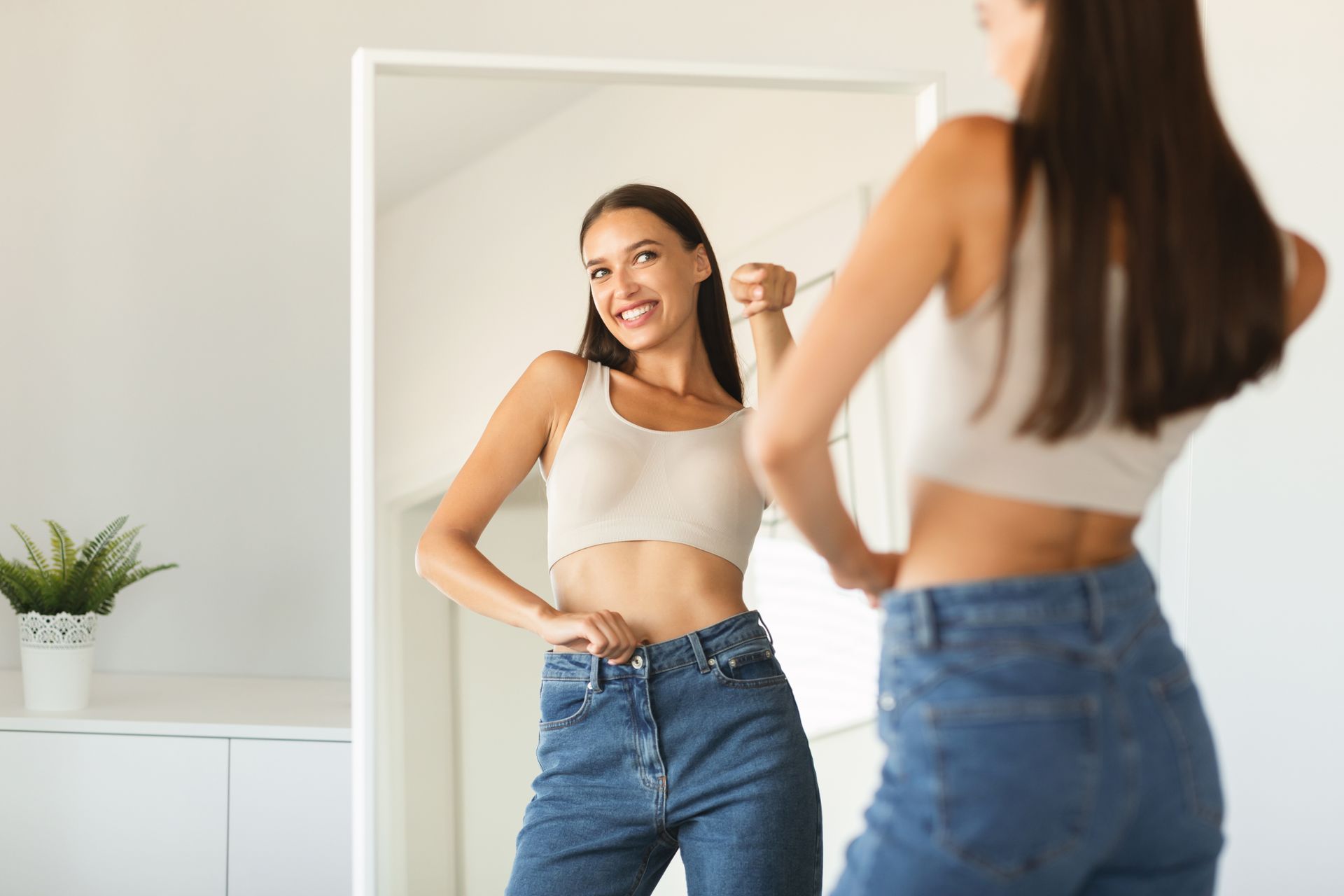 A woman is measuring her waist in front of a mirror.