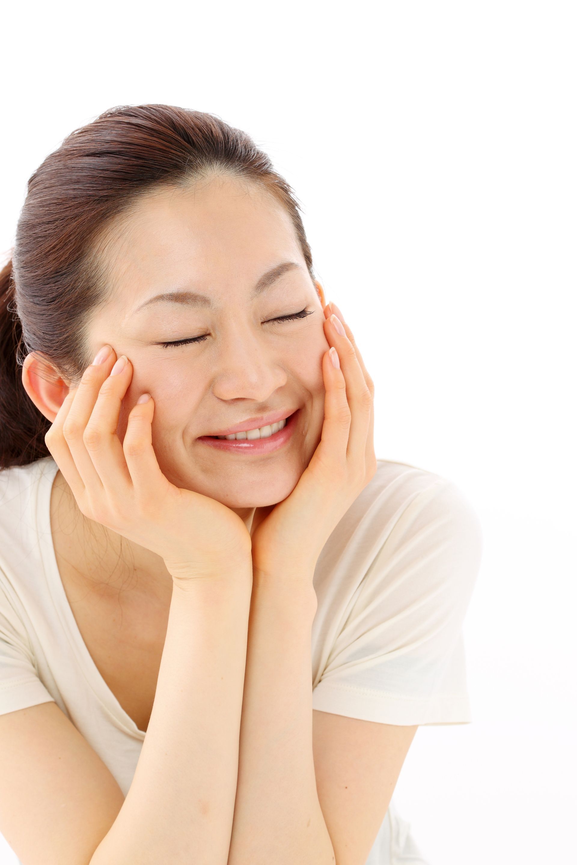 A woman is smiling with her hands on her face.