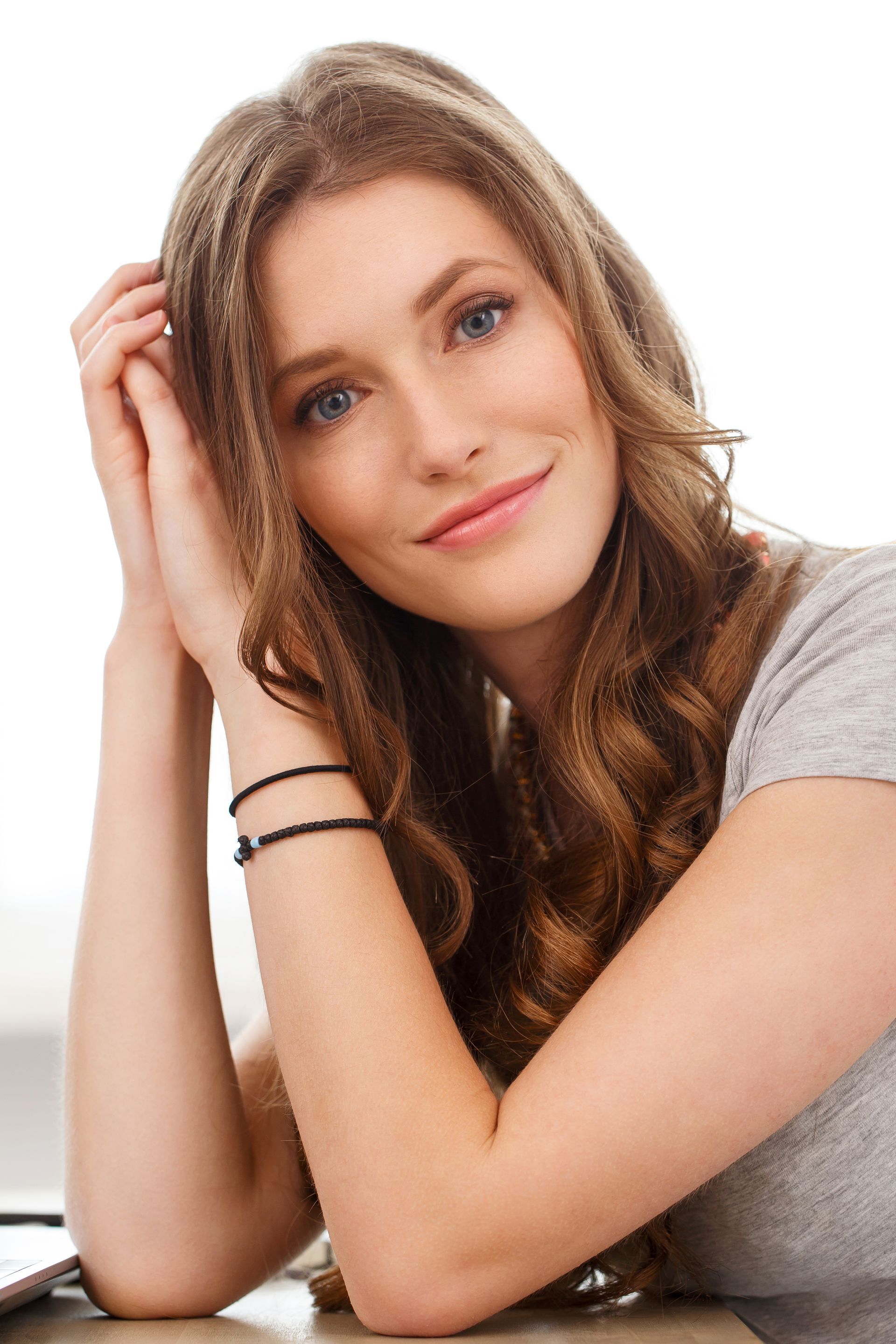 A woman with long hair is sitting at a table with her hands on her head.