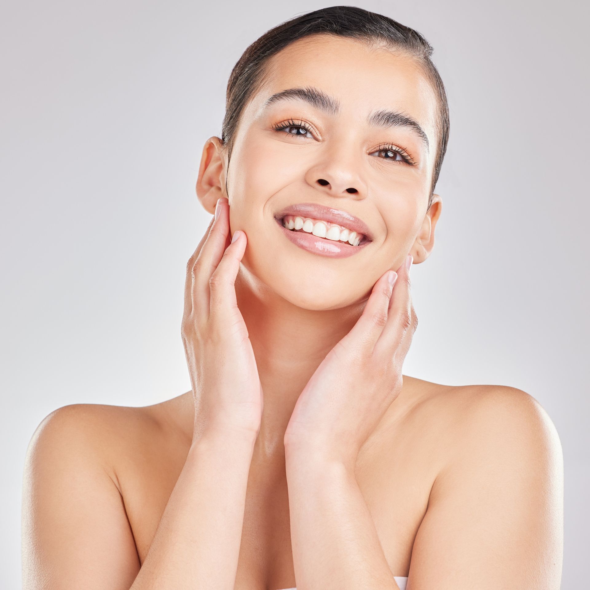 Smiling woman with hands on her cheeks, looking up; neutral background.