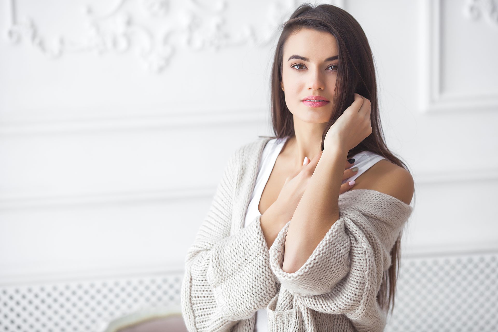 A woman in a sweater is standing in front of a white wall.