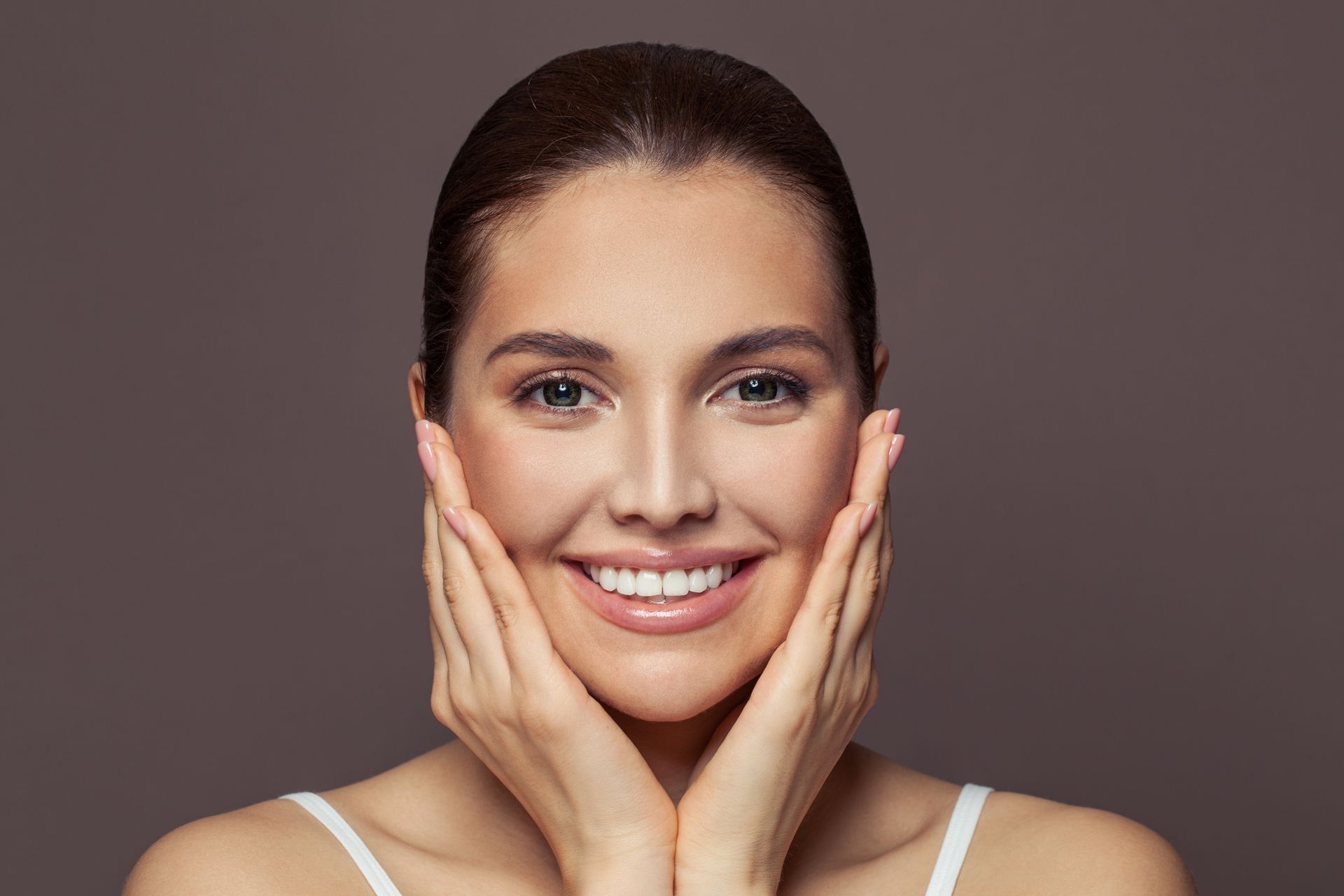 A woman is smiling and touching her face with her hands.