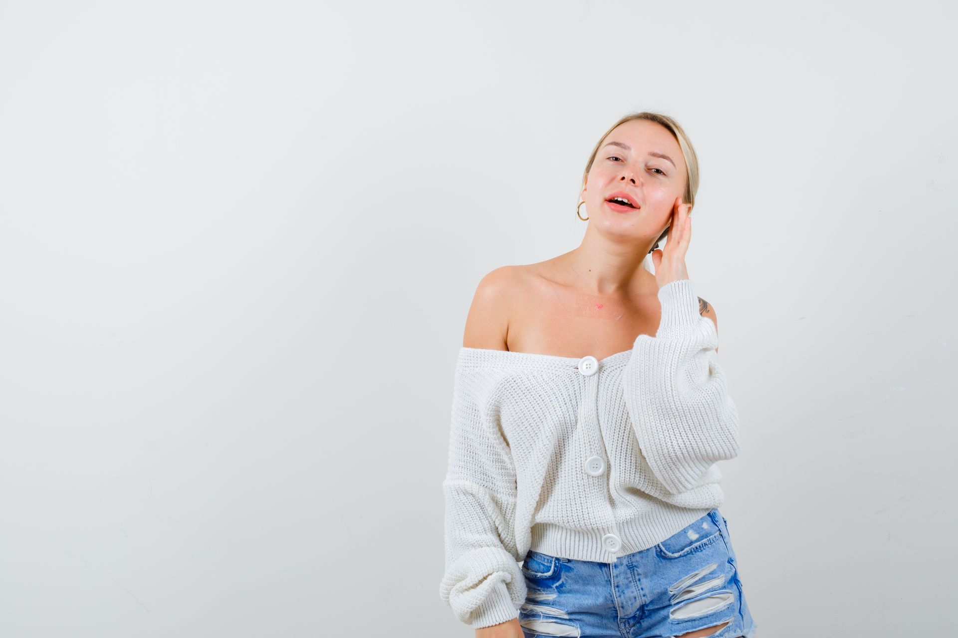 A woman in a white sweater and blue shorts is talking on a cell phone.