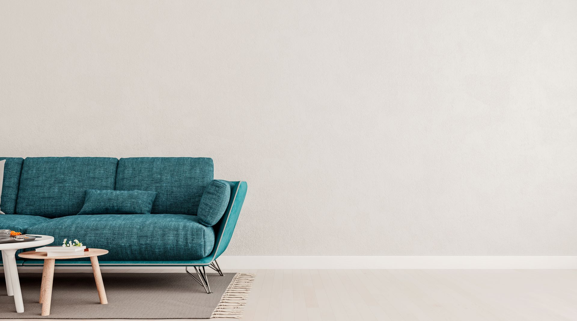 Teal sofa and small tables in front of a white wall, on a light floor.