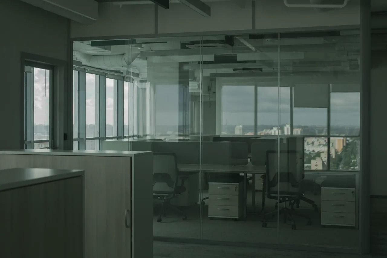 Empty office interior with glass walls, desks, and city views.