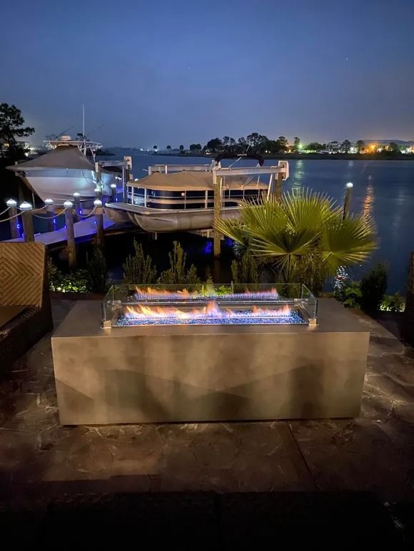 Fire pit with blue flames on a waterfront deck at dusk, with boats in the background.