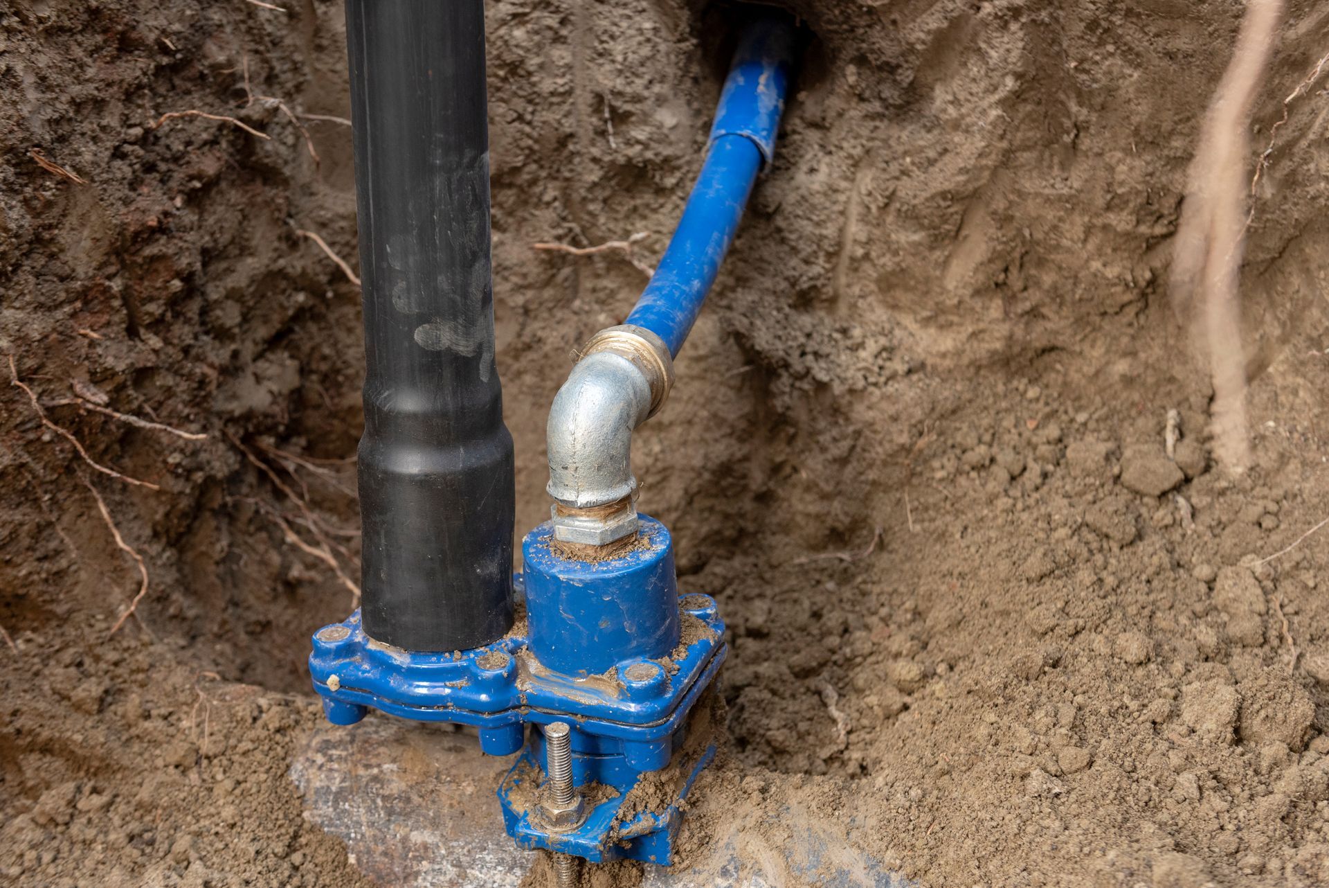 Blue and black water pipe assembly installed in a dirt trench.