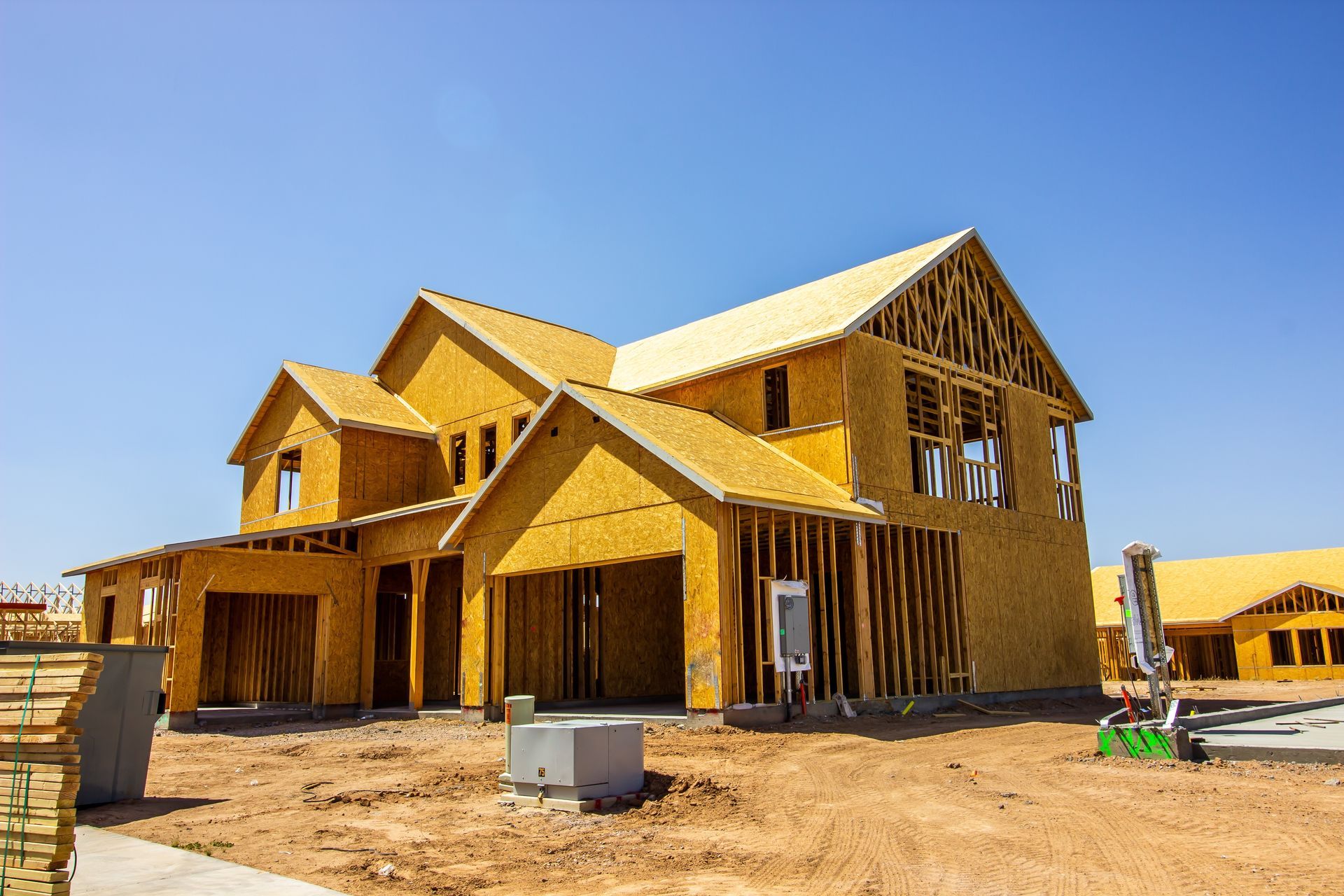 House under construction; wood frame, exposed beams, garage, bright blue sky.