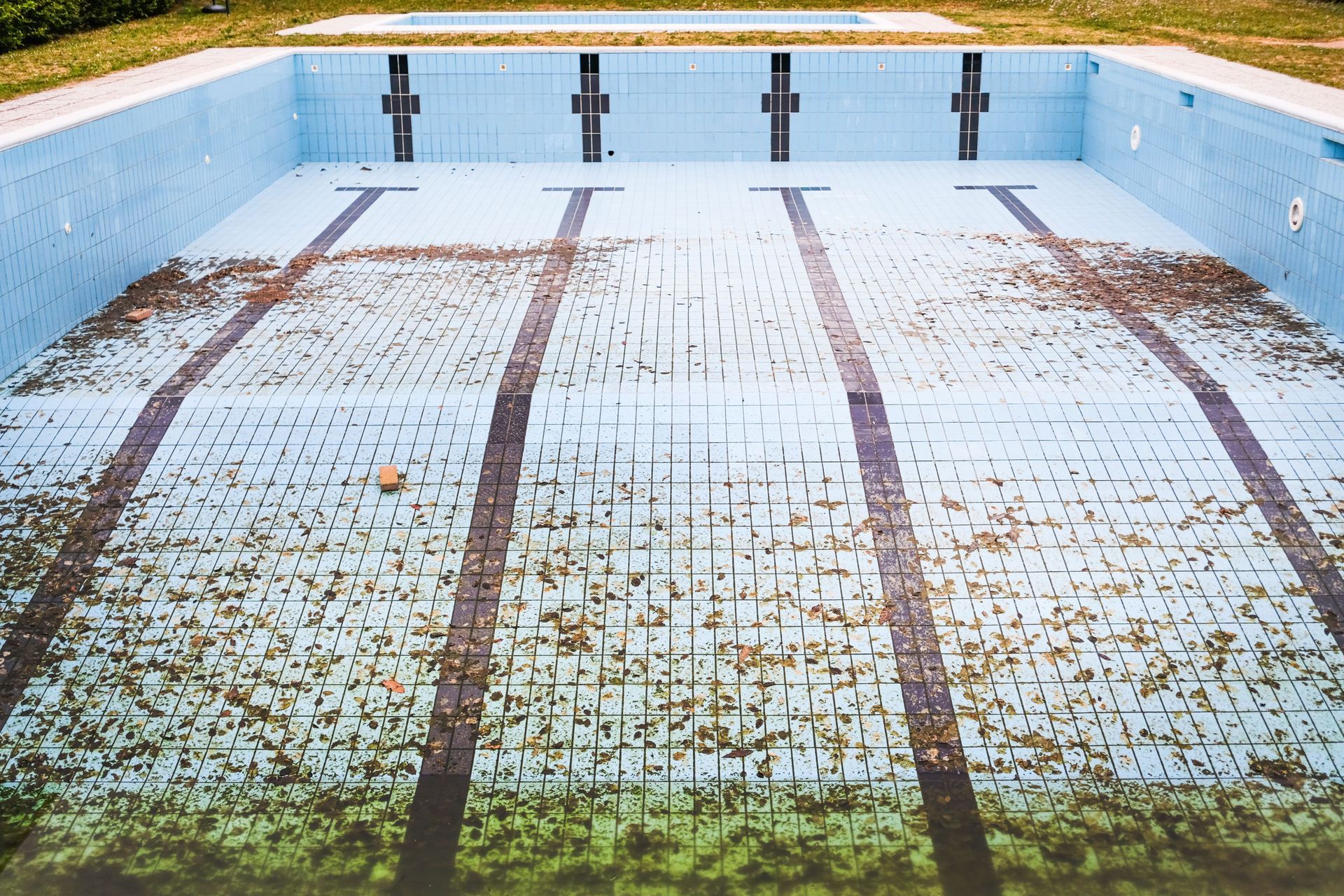 An empty, stained swimming pool with blue tiled walls and three dark lane lines.
