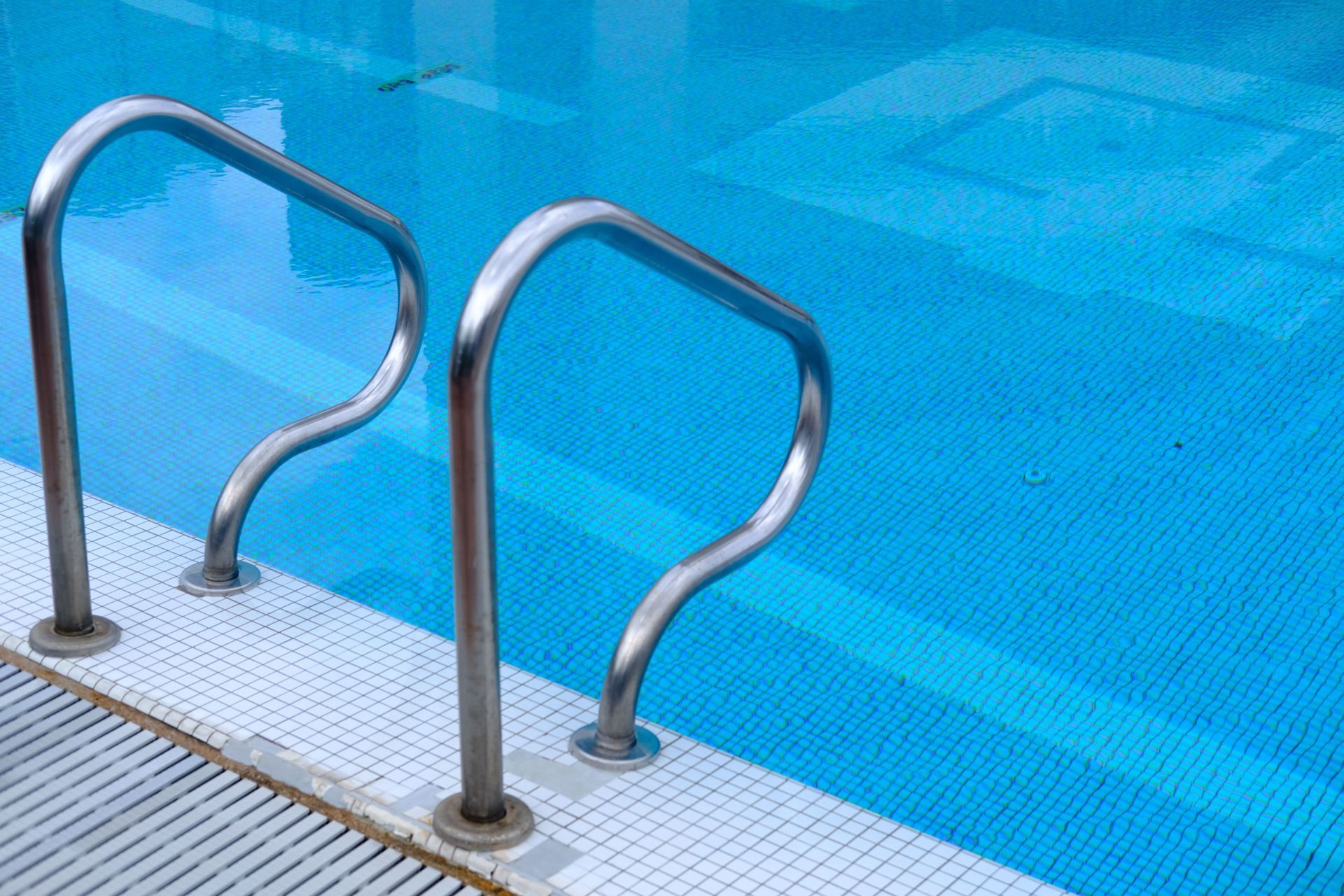 Stainless steel pool handrails beside a bright blue swimming pool edge