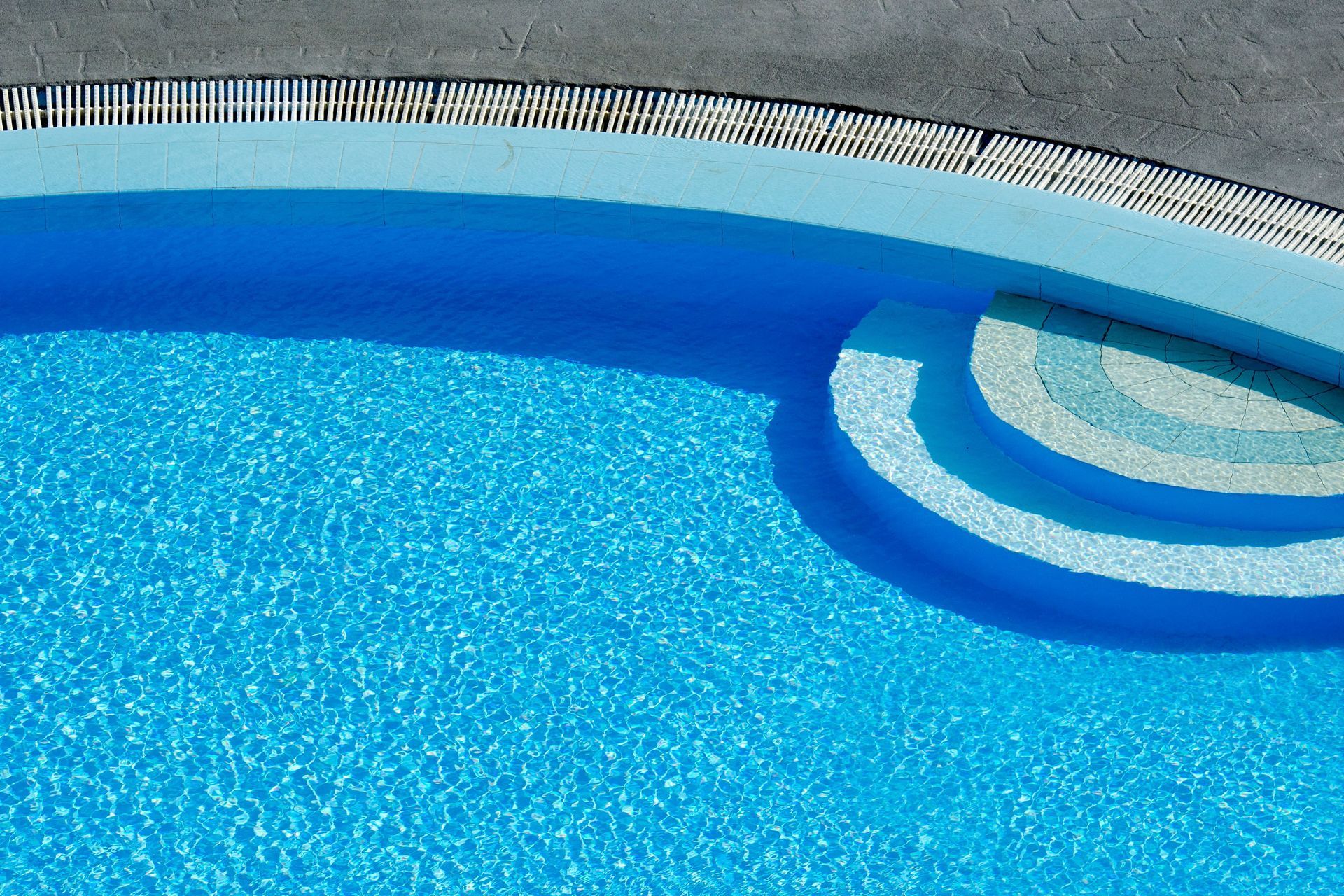 Blue swimming pool with curved steps and a white pool edge