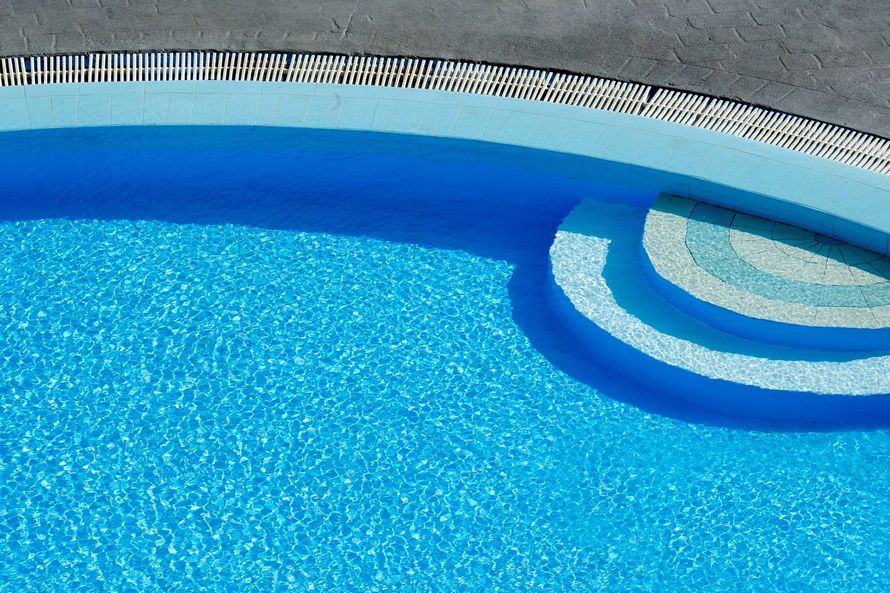 Blue swimming pool with curved steps and a white pool edge