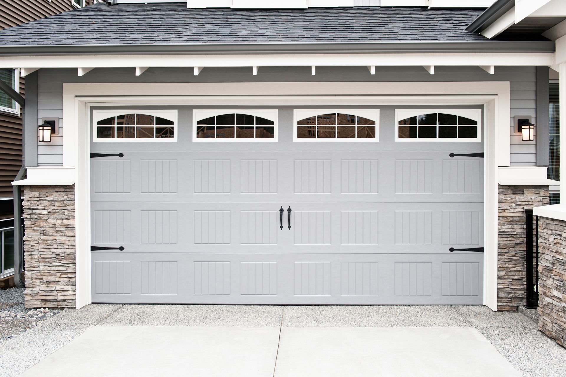 Gray garage door with decorative hardware, windows, and stone accents.