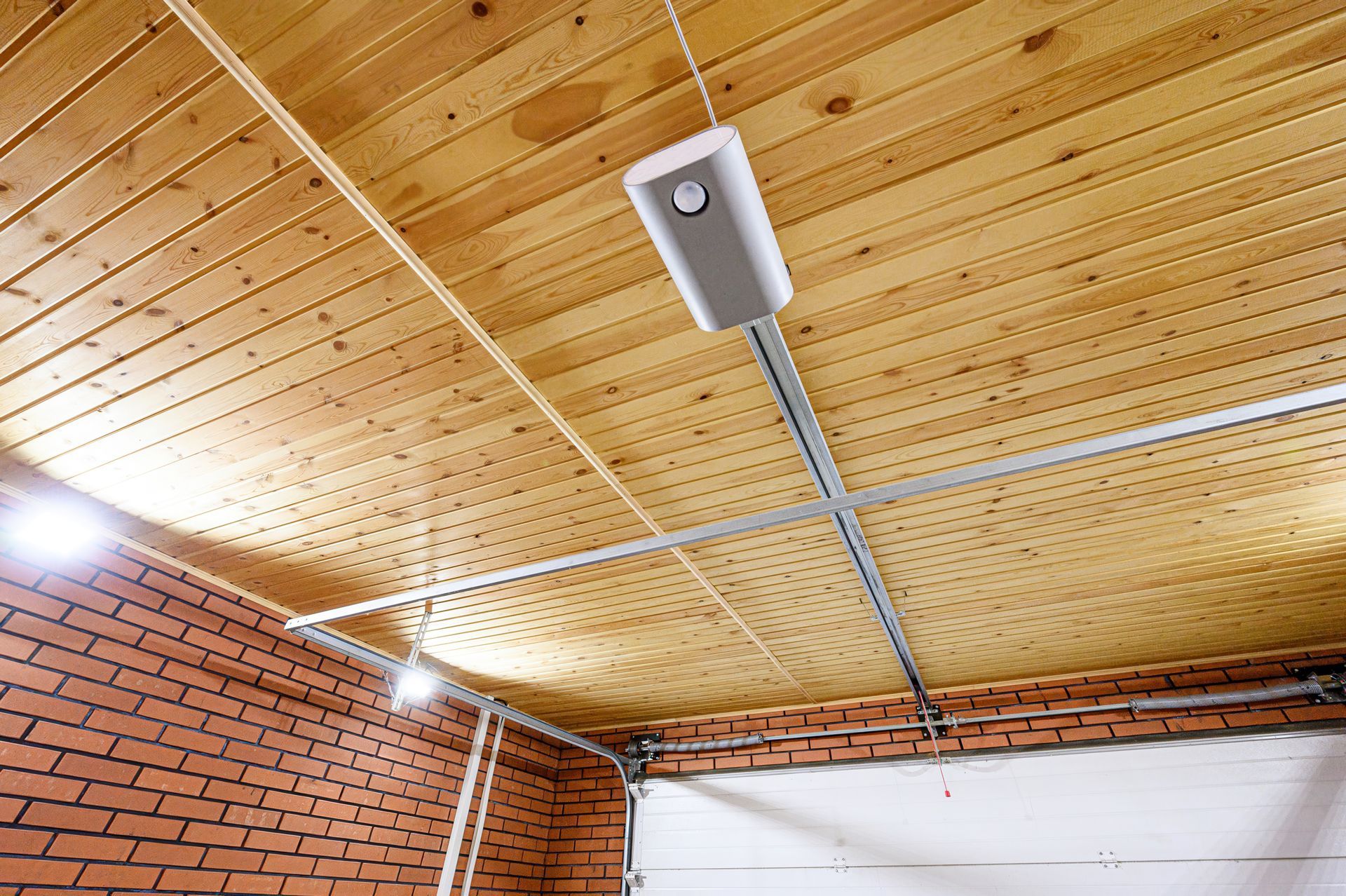 Garage ceiling with wooden planks, automated opener, and brick walls.