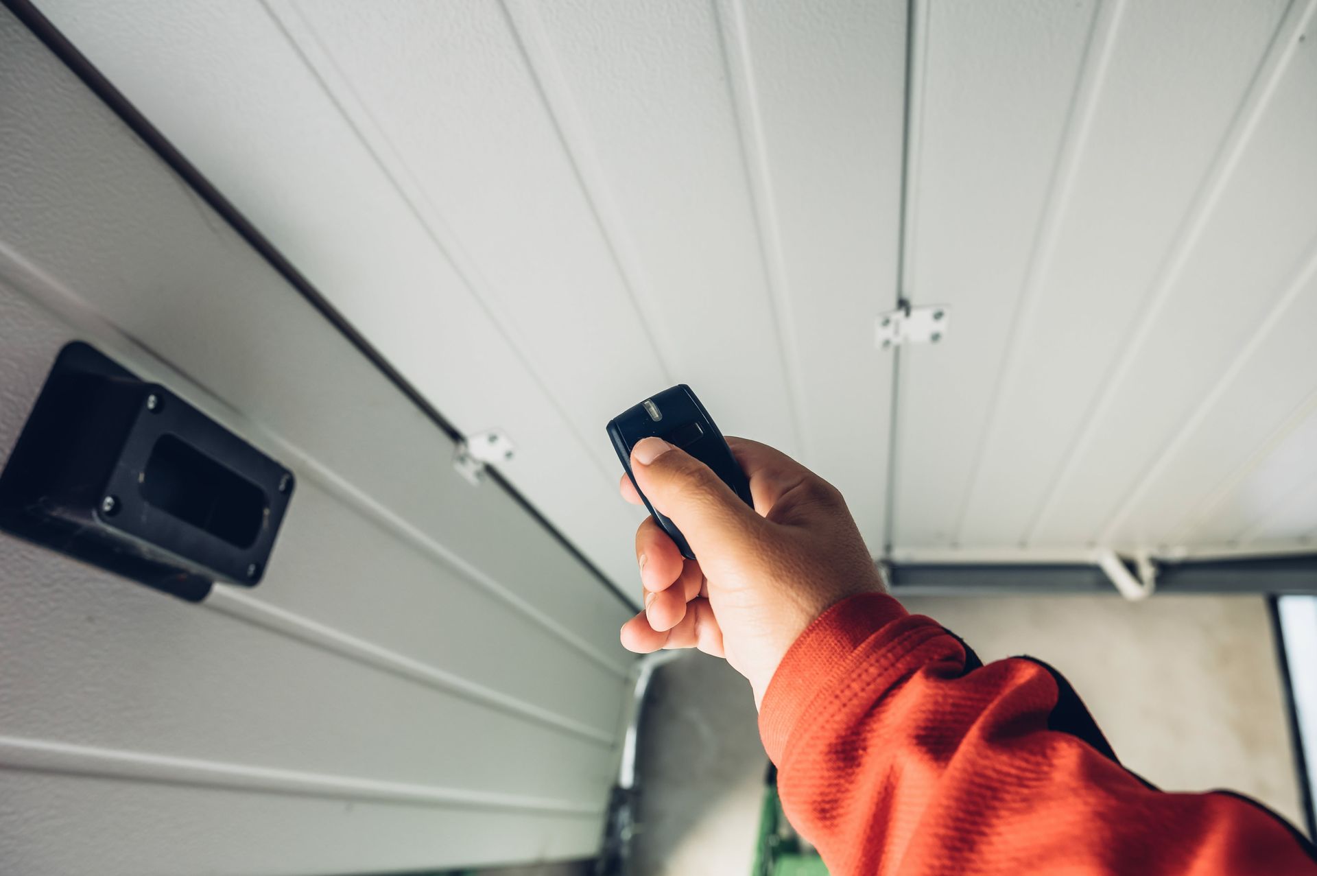 Hand holding a garage door opener, pointing it at the garage door track and motor.