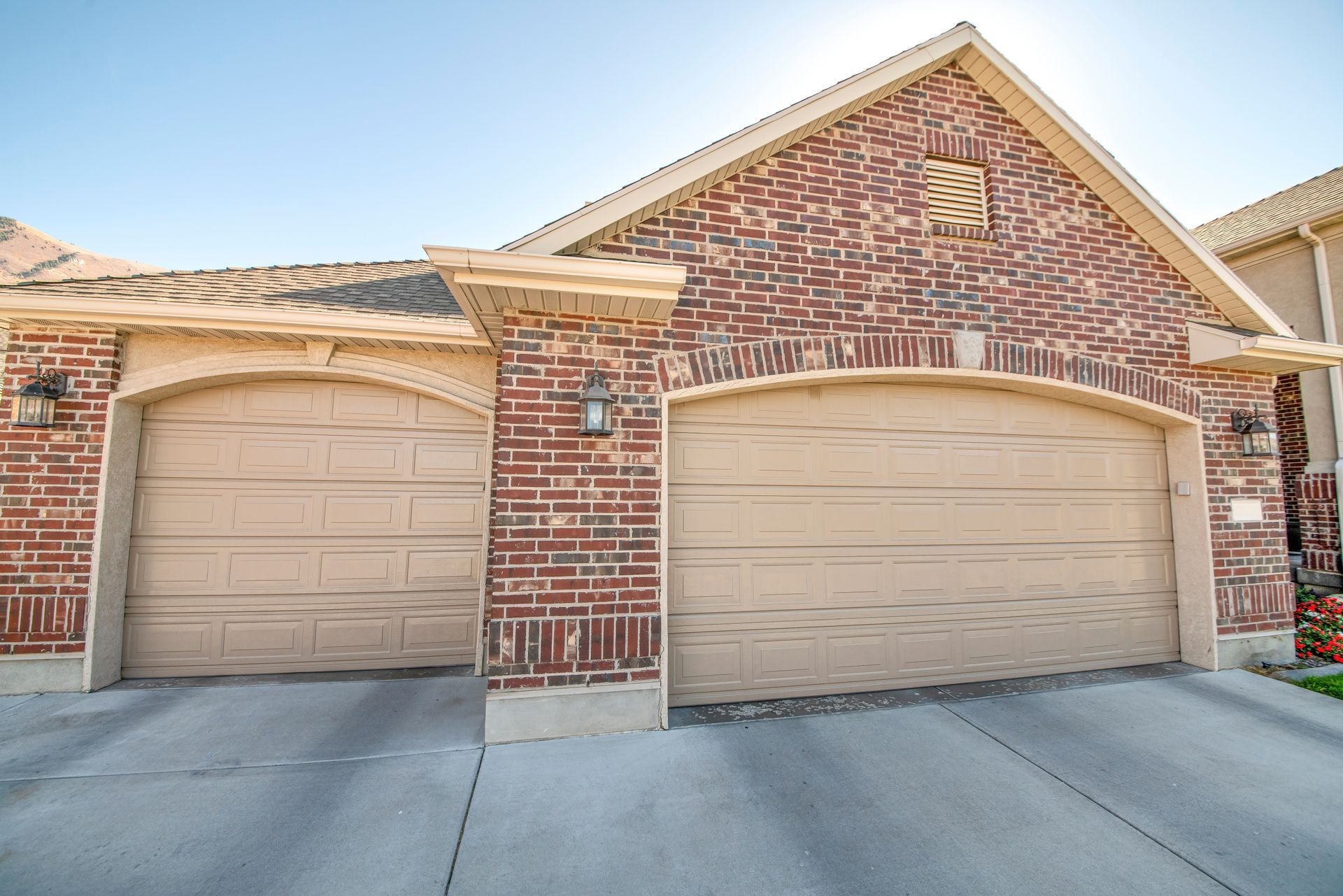 Tan garage doors with brick facade under a sunny sky.