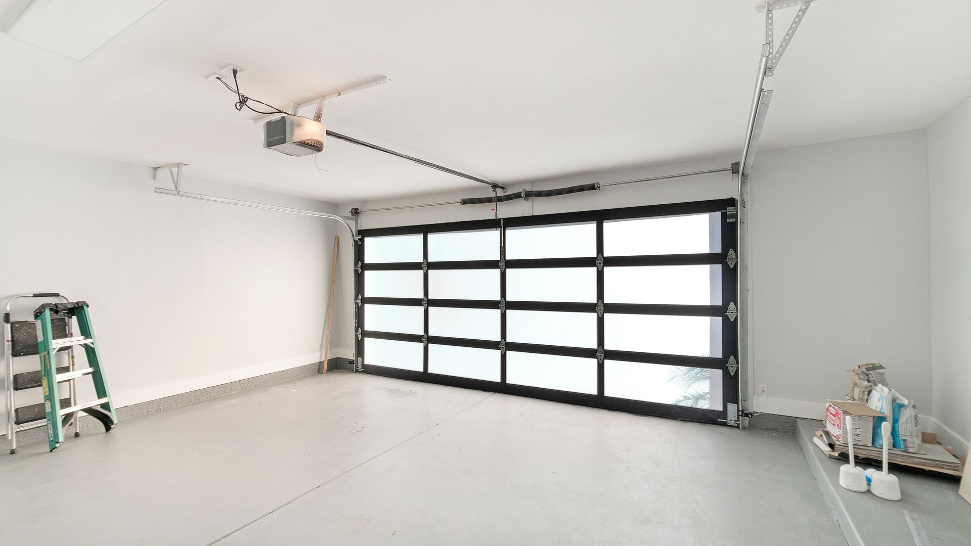 Empty, freshly painted garage with a glass-paneled garage door; a step ladder and cleaning supplies sit nearby.