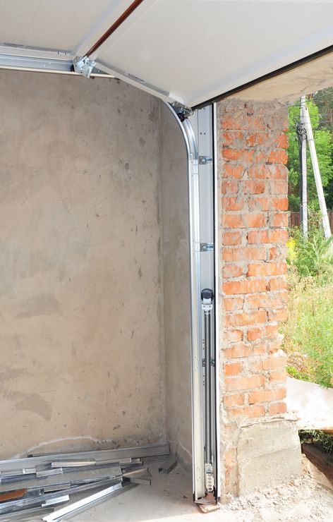 Garage door frame construction. Steel track attached to brick and concrete walls; interior view.