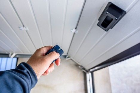Hand holding a garage door opener remote, activating a white overhead door.