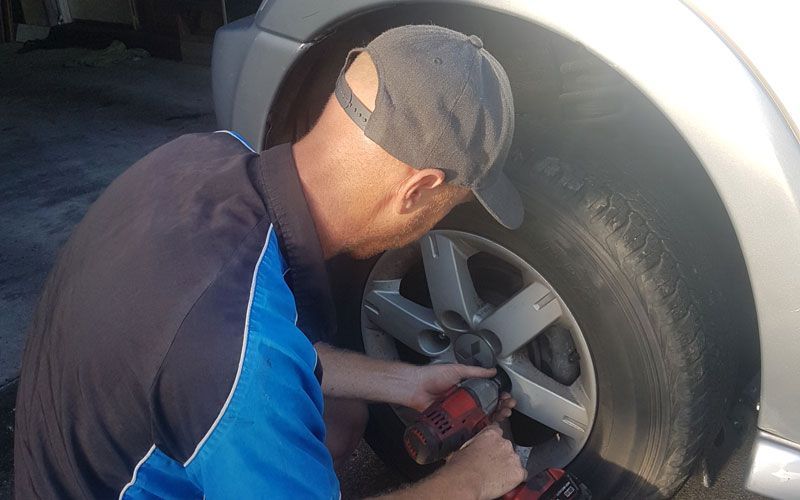 A Man Is Working on A Tire on A Car — Automotion Mechanical In Pacific Paradise, QLD