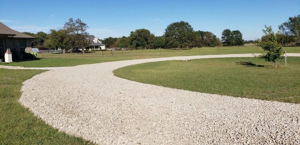 A gravel driveway leading to a house in a grassy field.