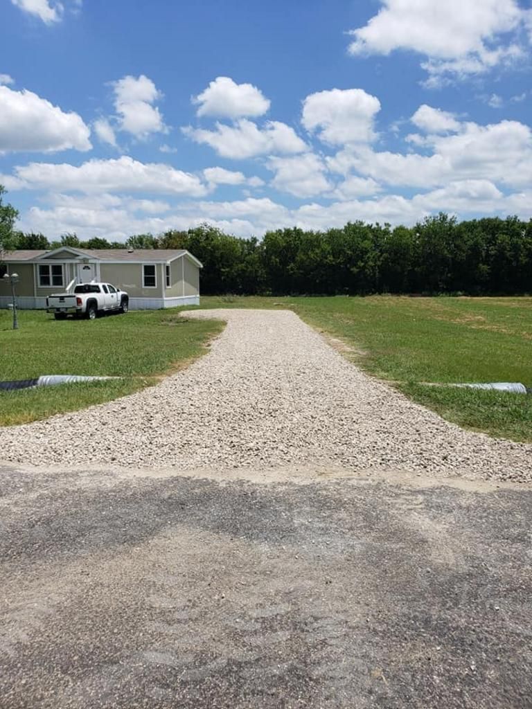 A white truck is parked on the side of a gravel road in front of a mobile home.