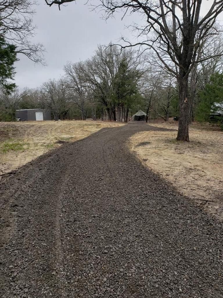 A gravel road going through a field with trees on both sides.
