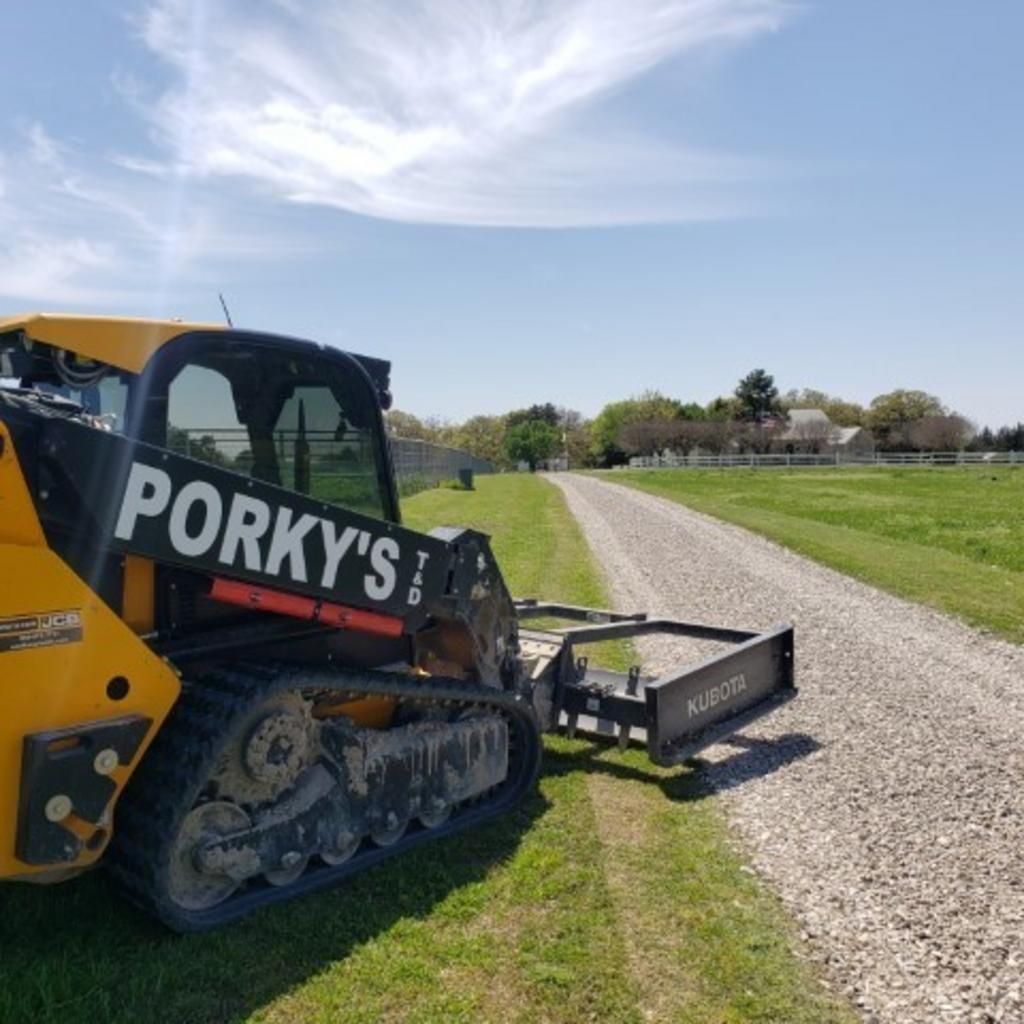 A yellow and black porky 's tractor is parked on the side of a gravel road.