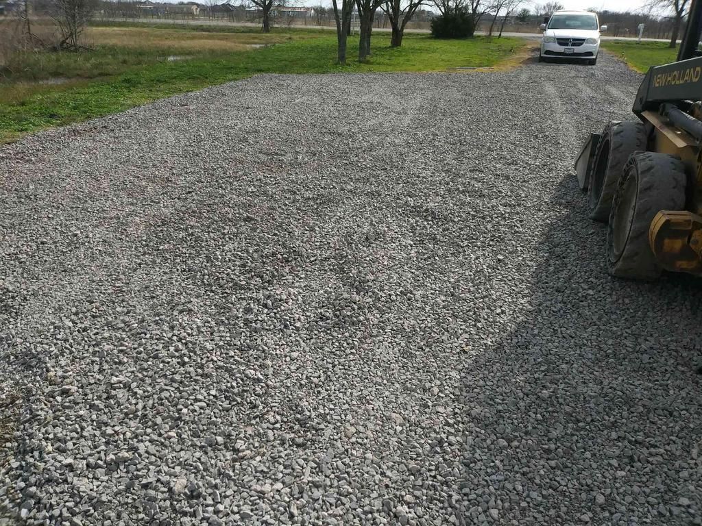 A car is parked in a gravel driveway next to a bulldozer.
