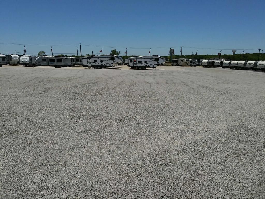 A lot of rv 's are parked in a gravel lot