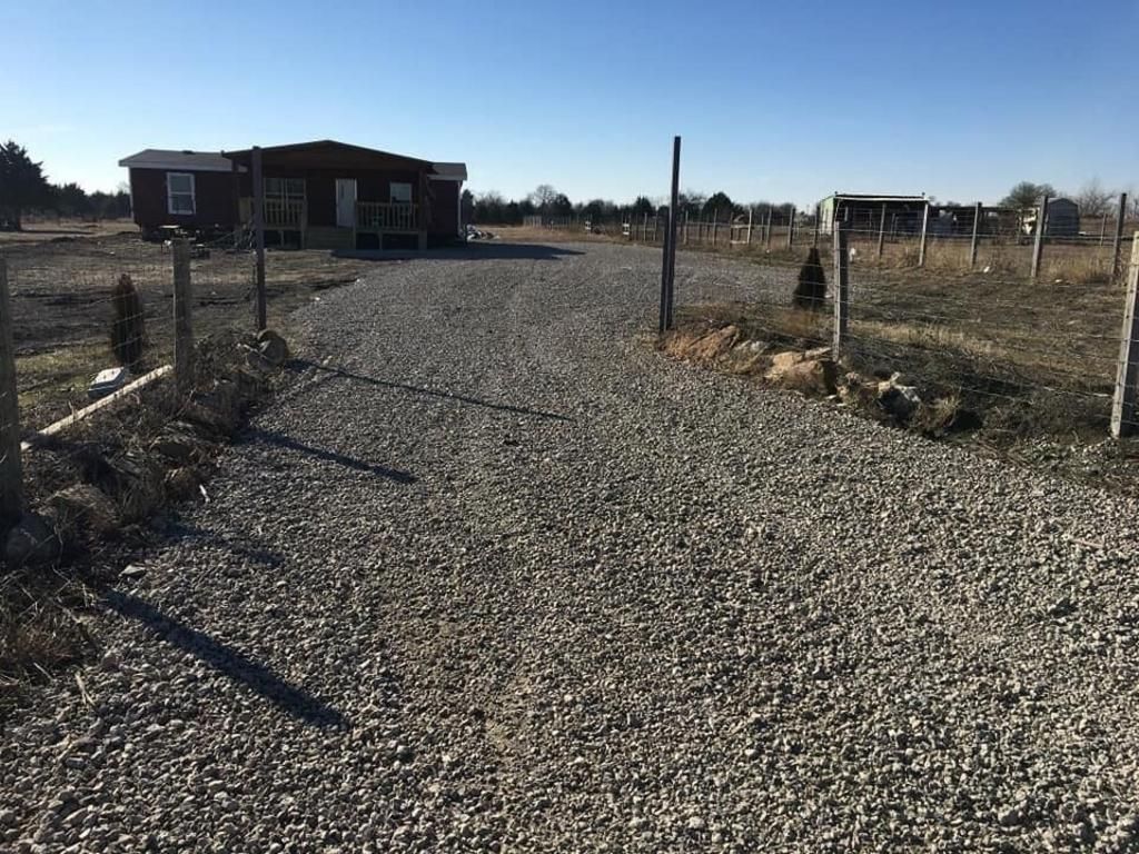 A gravel road leading to a house in the middle of a field.