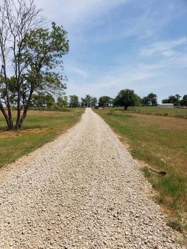 A gravel road going through a grassy field with trees on both sides.