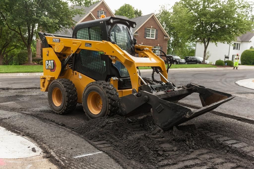 A yellow and black cat skid steer is driving down a street.
