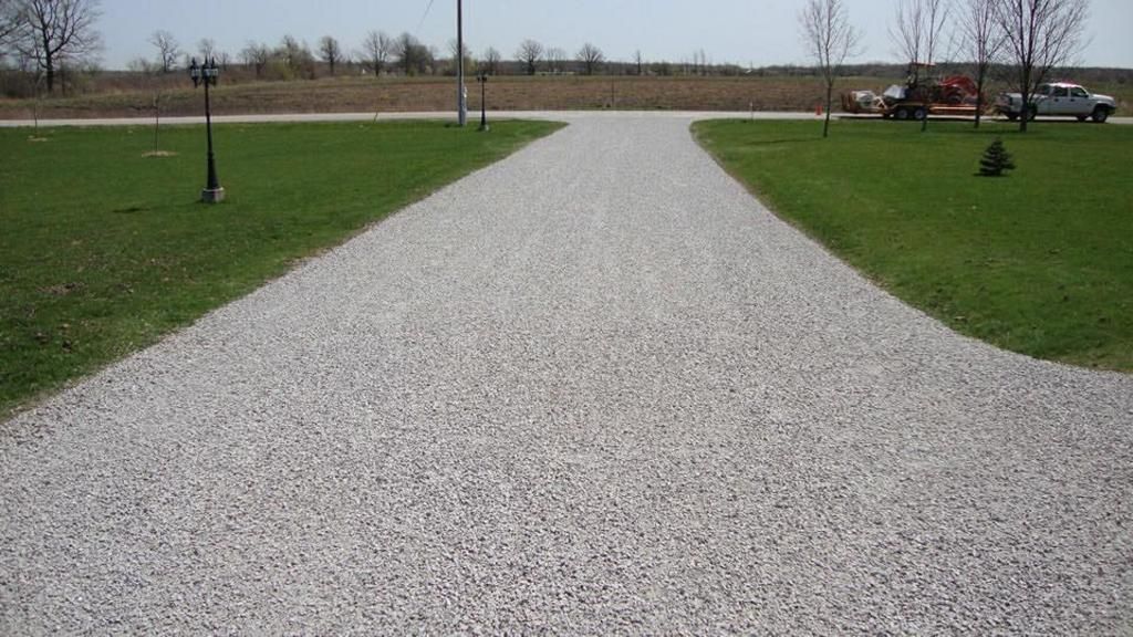 A gravel driveway going through a grassy field.