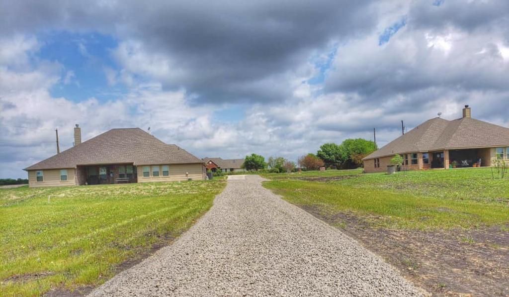 A dirt road leading to two houses on a cloudy day.