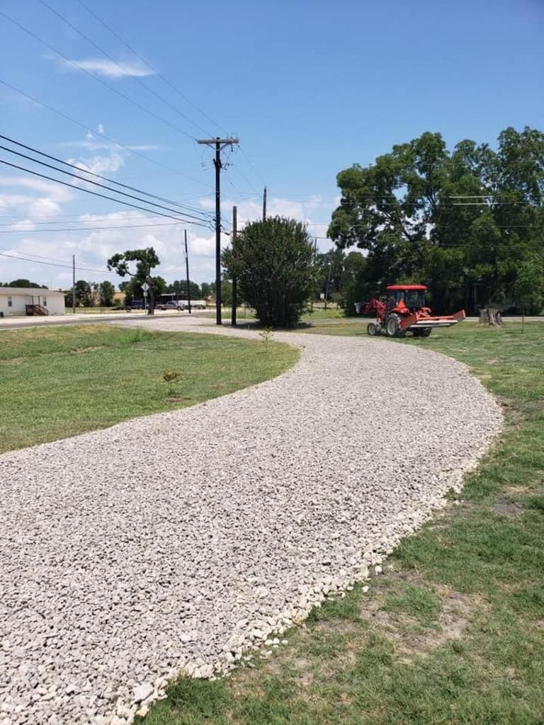A gravel driveway leading to a golf cart in a grassy field.