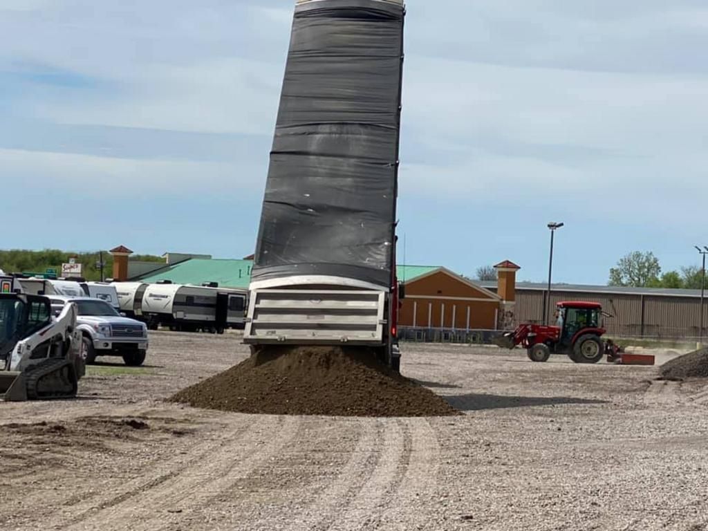 A dump truck is dumping dirt on a gravel road.