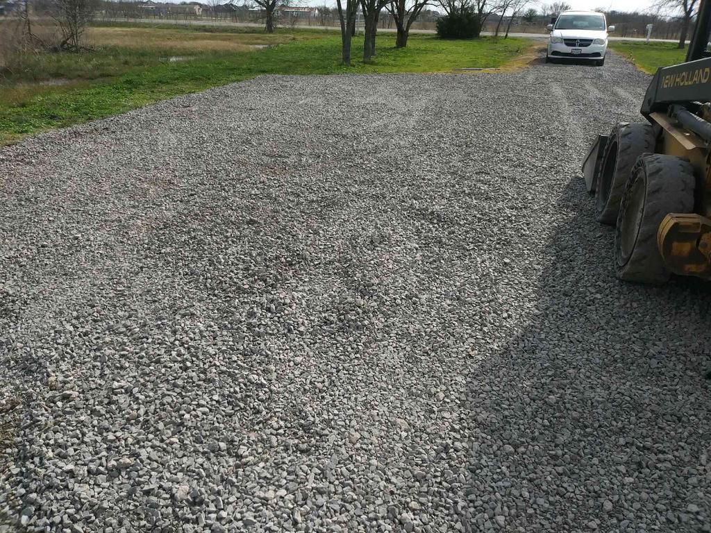 A white car is parked in a gravel driveway next to a bulldozer.