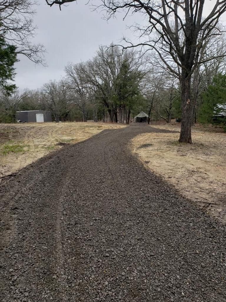 A gravel road going through a field with trees on both sides.