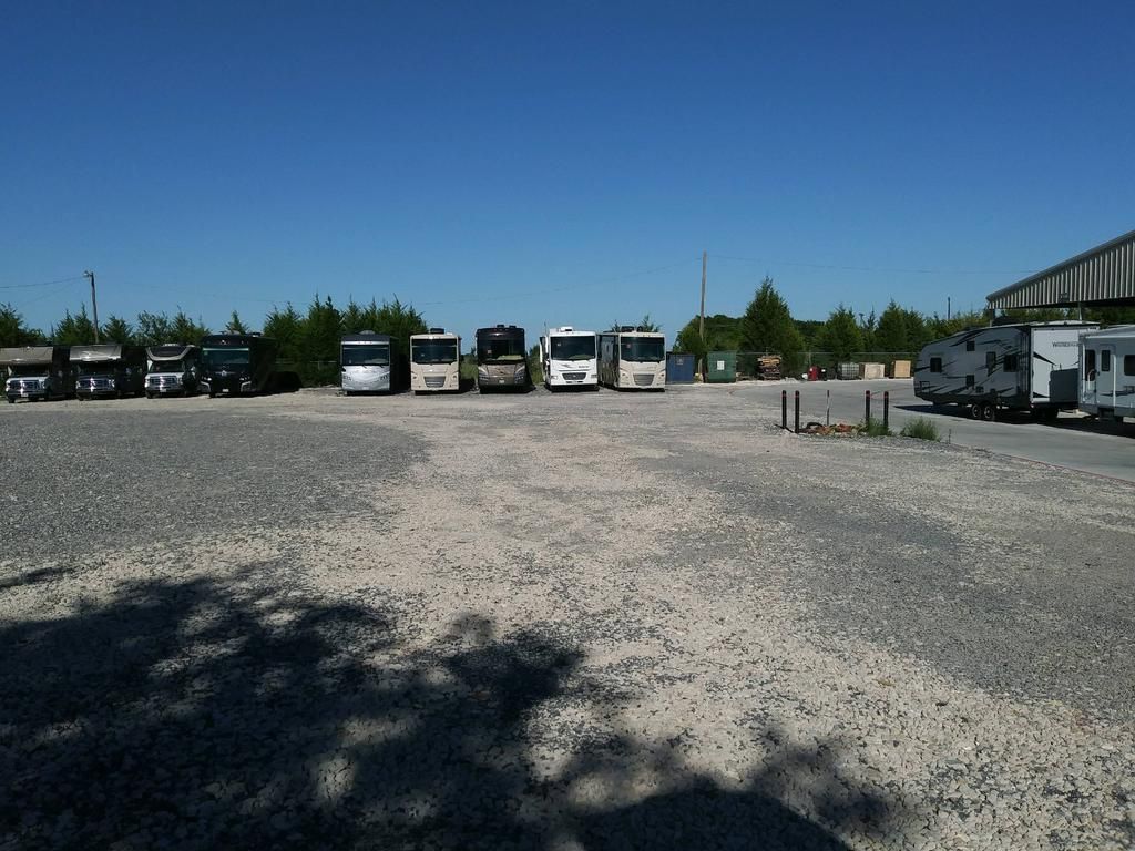 A row of rvs are parked in a gravel lot